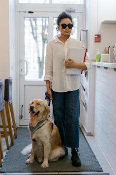 Blind woman with guide dog standing indoors, holding a book.